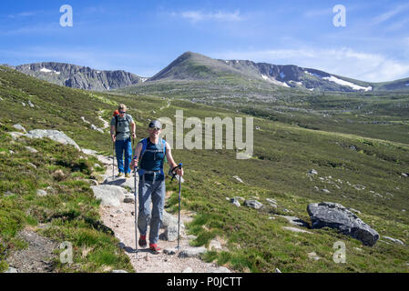 Due hillwalkers / alpinisti con bastoncini e zaini discendente del percorso di montagna in primavera nel Parco Nazionale di Cairngorms, Highland, Scozia Foto Stock