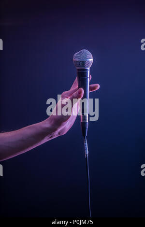 Mano con microfono su uno sfondo nero, il concetto di musica, bella illuminazione sul palco Foto Stock