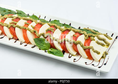 I pomodori tagliati grossolanamente con formaggio, su una piastra quadrata su uno sfondo bianco . Snack freddi Foto Stock