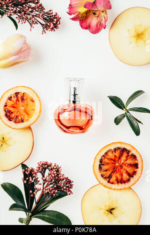 Vista superiore della bottiglia di profumo circondato con frutti e fiori su bianco Foto Stock