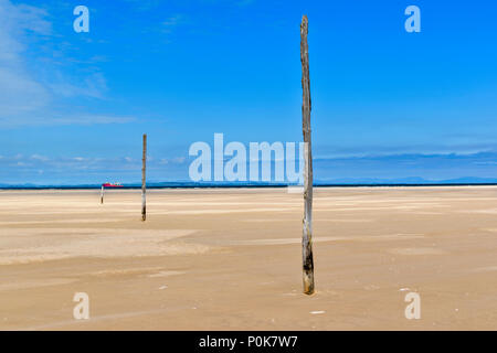 Spiaggia di CULBIN MORAY Scozia miglia di spiaggia di sabbia con il mare in lontananza la nave rossa sull'orizzonte e tre pali di legno Foto Stock