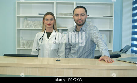 Amichevole maschio e femmina infermieri dietro il banco di ricevimento in ospedale Foto Stock