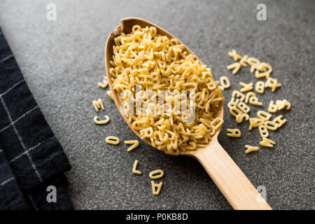 Materie non cotti alfabeto di pasta a cucchiaio di legno. Alimenti biologici. Foto Stock