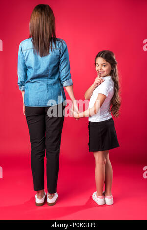 Figlia di madri tenendo la mano e mostrando il silenzio segno su rosso Foto Stock
