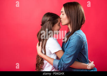 Madre baciare la figlia a fronte isolato su rosso Foto Stock