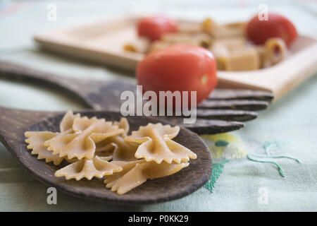 Integrale di farfalle di pasta su un mestolo di legno e freschi pomodori ciliegia Foto Stock