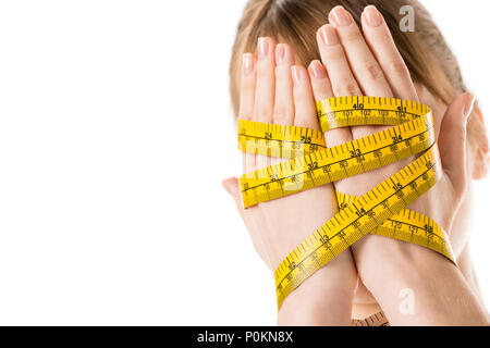 Close-up shot di donna che ricopre la faccia con le mani legate in nastro di misurazione isolata su bianco Foto Stock