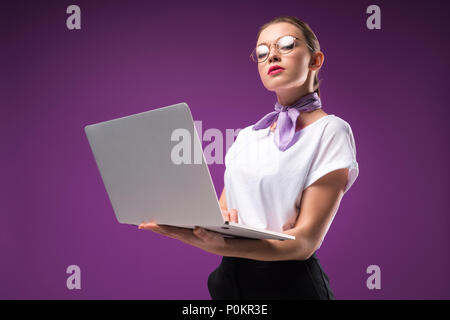 Ragazza con laptop e guardando la telecamera isolata su viola Foto Stock