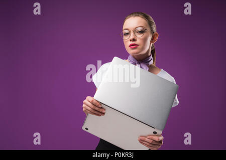 Ragazza con laptop e guardando la telecamera isolata su viola Foto Stock