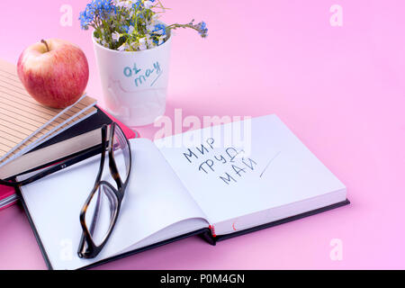 Fiori blu e libri. Aprire il blocco note e bicchieri. Atmosfera di lavoro. Vacanza di lavoro in maggio. Il testo. Sfondo rosa. Foto Stock