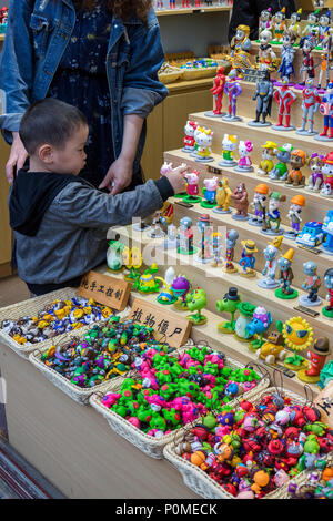 Yangzhou, Jiangsu, Cina. Little Boy esaminando le piccole statuette in un negozio di Dong Guan Street. Foto Stock