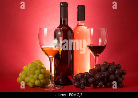 Composizione con vino rosso e bianco di bottiglie, uva un bicchieri. Su sfondo rosso Foto Stock