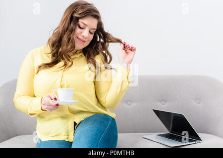 Ritratto di donna con la tazza di caffè seduti sul divano con il portatile a casa Foto Stock