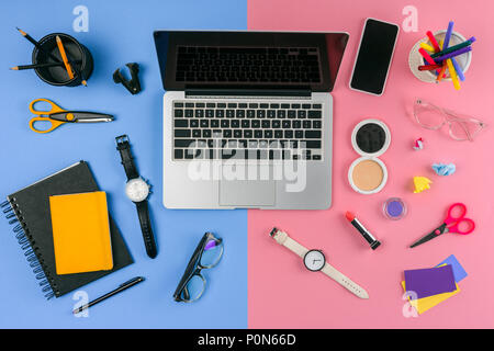 Vista superiore del laptop, smartphone e cosmetici con forniture per ufficio diviso a maschio e femmina workplace Foto Stock