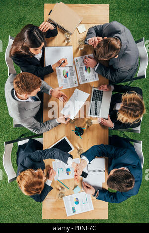 Vista dall'alto di colleghi di lavoro avente incontro a tavola con i documenti e i dispositivi in ufficio Foto Stock