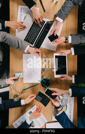 Vista ritagliata di colleghi di lavoro che mostra i dispositivi digitali per ogni altro a tavola in ofifce Foto Stock