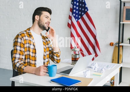 Giovani freelance di bere il tè e a parlare su smartphone in ufficio di luce Foto Stock