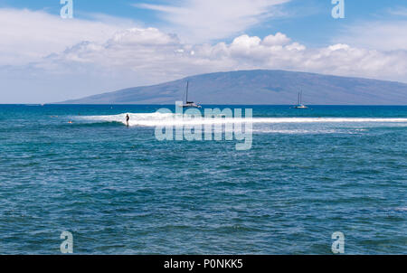 Surfista che cattura una piccola onda al largo di Maui con l'isola di Lana'i sullo sfondo. Foto Stock