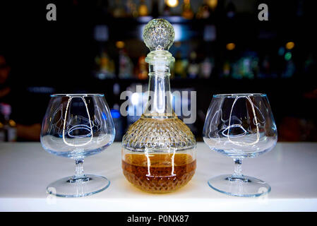 Decanter in vetro con alcool e due bicchieri su sfondo scuro della barra. Foto Stock