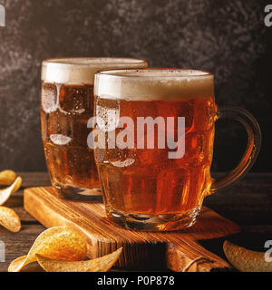 La birra. Birra fredda in vetro con chip su uno sfondo scuro. Foto Stock