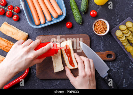 Foto nella parte superiore della tabella con ingredienti per hot dogs, tagliere, mani dell'uomo Foto Stock