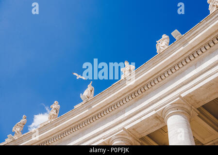 Vista dal basso di uccelli che volano sopra le statue in Piazza San Pietro in Vaticano, Italia Foto Stock