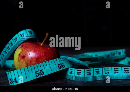 Concetto di dieta. Apple rosso blu con nastro di misurazione su scuro dello sfondo Moody Foto Stock