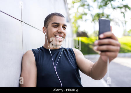 Sorridente giovane americano africano uomo in auricolari tenendo selfie con lo smartphone Foto Stock