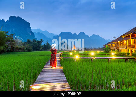 Giovane donna camminando sul percorso di legno verde con campo di riso in Vang Vieng, Laos. Foto Stock