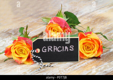 Gracias (grazie in spagnolo) scritto su mini lavagna con tre rose colorata su una superficie di legno Foto Stock