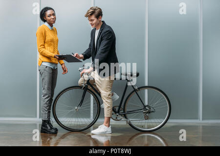 Giovane imprenditore firma contratto in mani del giovane americano africano collega mentre era seduto sulla bici Foto Stock