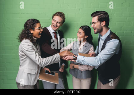 Emozionato multietnica team business tenendo le mani insieme nella parte anteriore della parete verde Foto Stock