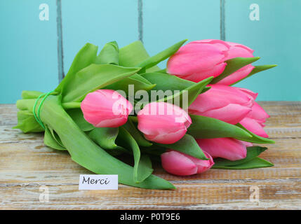 Merci (grazie in francese) card con rosa tulip bouquet rustico sulla superficie di legno Foto Stock