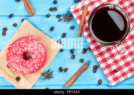 Tazza di caffè nero con un fiocco rosa e granuli disseminati su un sfondo di legno, vista dall'alto Foto Stock