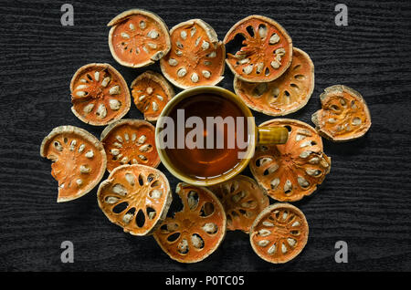 Le erbe aromatiche essiccate e secchi Frutta bael, vista dall'alto di bael asciutto e bicchiere di tè e succhi bael sul pavimento di legno, fette di frutta bael sul tavolo scuro. Foto Stock