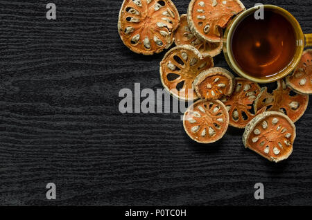 Le erbe aromatiche essiccate e secchi Frutta bael, vista dall'alto di bael asciutto e bicchiere di tè e succhi bael sul pavimento di legno, fette di frutta bael sul tavolo scuro. Foto Stock