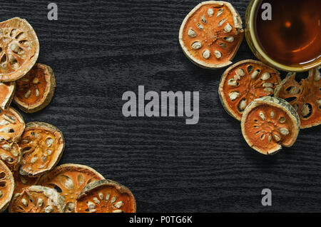 Le erbe aromatiche essiccate e secchi Frutta bael, vista dall'alto di bael asciutto e bicchiere di tè e succhi bael sul pavimento di legno, fette di frutta bael sul tavolo scuro. Foto Stock