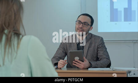 Professional insegnante maschio spiegando le idee principali del saggio rendendo la discussione tra gli studenti a porre domande e condividere consulenze durante la lezione di formazione in aula Foto Stock