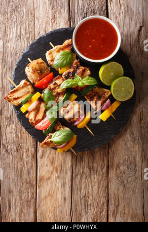 Hot pollo grigliato kebab spiedini con verdure colorate con salsa, basilico e calce closeup sul tavolo. Verticale in alto vista da sopra Foto Stock