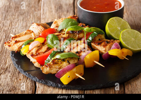 Servito pollo grigliato kebab spiedini con verdure con salsa di erbe e di calce closeup su una piastra di ardesia su una tavola orizzontale. Foto Stock