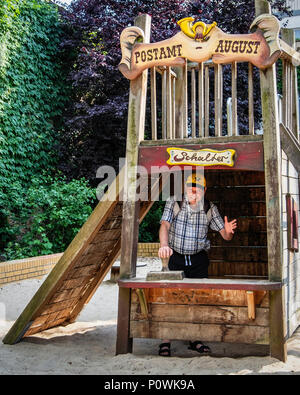 Berlin Mitte Auguststrasse Parco per bambini. Senior uomo in giallo tedesco post pac e Kiddies Post Office & buca di sabbia Foto Stock