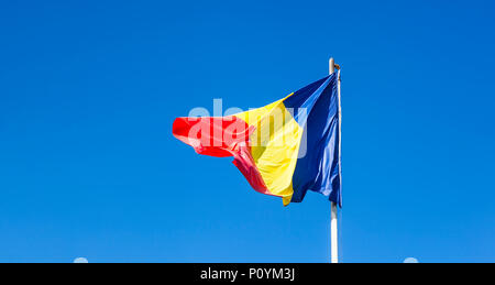 Bandiera rumena sul montante. Bandiera della Romania di seta. Bandiera rumena sul pennone soffiando nel vento isolata contro il cielo blu con copyspace. Foto Stock