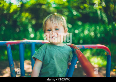 Un sorridente ragazzino è seduto su un merry-go-round nel parco Foto Stock