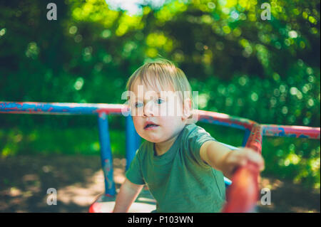 Un grazioso piccolo ragazzo è seduto su un merry-go-round nel parco Foto Stock