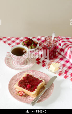 Colazione a base di pane, toast con burro e fragole e rabarbaro marmellata, servito con tè. In stile rustico, il fuoco selettivo. Foto Stock
