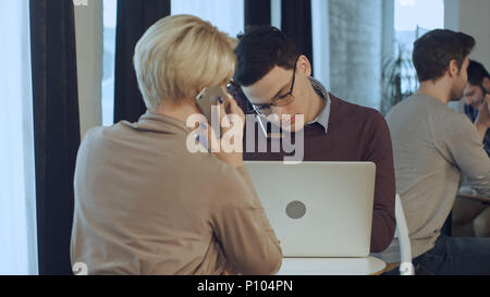 Due colleghi che lavorano insieme, avente le chiamate telefoniche in cafe Foto Stock