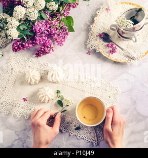 Vista superiore della donna di mani vintage tazza di tè verde e spiraea ramo sul tavolo di meringa dolci, un bouquet di fioritura lilla e spiraea Foto Stock