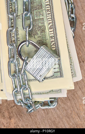 Centinaia di dollari di banconote è fissato con una catena e un lucchetto. Close up. In legno marrone dello sfondo. Foto Stock