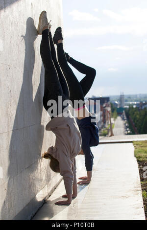 Due giovani donne acrobat facendo handstand sulla parete con il paesaggio sullo sfondo Foto Stock