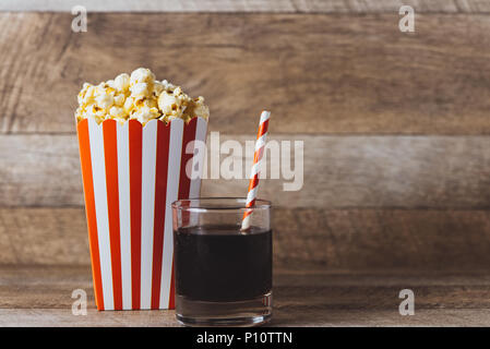 Il Popcorn in rosso e cartoncino bianco con soda sul tavolo di legno. Foto Stock
